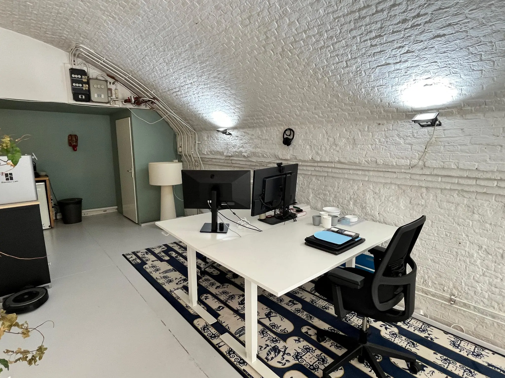 Kantoorruimte met witte gewelfde bakstenen muren, ingericht met een modern bureau en twee computerschermen.